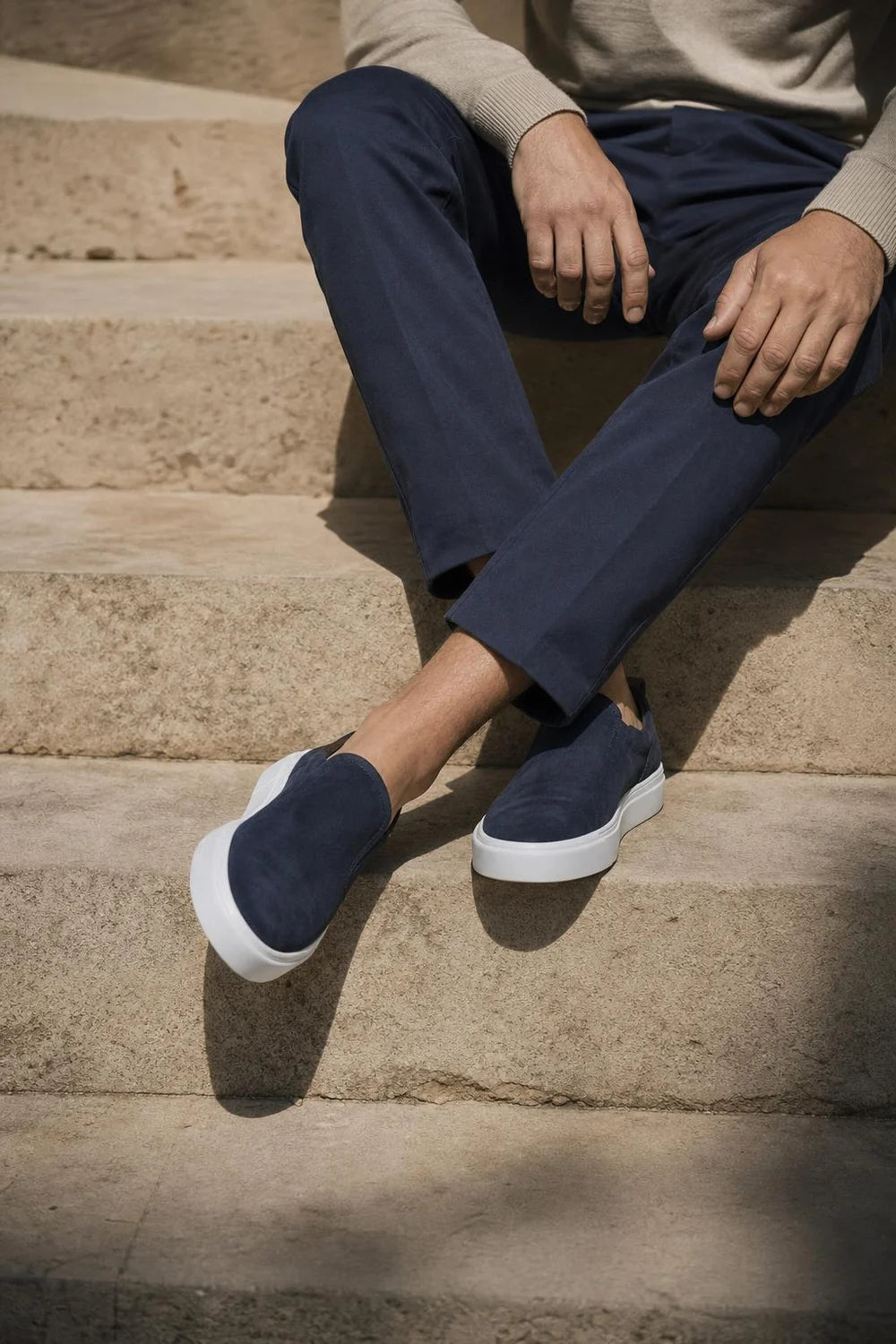 Marbella Suede Slip-On in navy, seated on stone steps